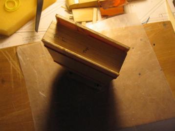 02-22-14: I used epoxy to glue the sides to the base.&nbsp;  The base
has the mounting holes already drilled to match the holes in the
wing.<br><br>

[The holes in the wing are another story.&nbsp;  In several of the
other photos you can see the sticks of spruce that I shaped and glued
to the top and bottom of the wing.&nbsp; These sticks have holes in
them for the bolts to mount the pod.&nbsp; The bolts pass through the
wing and secure with nuts on the bottom side.&nbsp; For strength and to
make it easier to put the bolts through the holes each of the four
pairs of holes (top and bottom) has a straight piece of brass tube
connecting them.&nbsp; The brass tube is glued into the spruce on the
top and bottom and passes through the wing.&nbsp; The spruce and brass
tubes were already installed, since I had used them to mount the pod
for the Black Widow .049 which was in use before I converted to
electric power.]<br><br>

And I marked in pen on the base lines showing where the sides should
attach.&nbsp; There isn't much room for mistakes here, because the pod
sides just fit between the holes.&nbsp; I didn't plan it that way--I
got lucky: The diameter of the motor and heat sink plus the thickness
of the two sides equals a distance just less than the space between the
edges of the mounting holes.<br><br>

The trick in attaching the sides to the base is to get everything
straight, parallel and perpendicular.&nbsp; To do this, I made a balsa
spacer from three pieces of 1/16" balsa.&nbsp; I cut them slightly over
the desired width, 0.875", then I carefully sanded them down, checking
with a caliper, until they were 0.875".&nbsp; It went something like that
anyway.&nbsp; I assembled the three pieces into an I shape.&nbsp; the I
was about 2.5" high and about 3.0" wide.<br><br>

[Actually, I found it necessary to cheat a little.&nbsp; I reduced the
width of the front end of the lower piece of wood in the "I" to 0.855". 
That allowed me to make that portion of the pod have sides that were
slightly closer together.&nbsp; I needed that because the front holes
in the wing were slightly closer together.]<br><br>

This I-shaped spacer was then rubber banded firmly between the two
sides.&nbsp; After trial fitting and checking that the fit was correct
I then applied epoxy to the base and carefully placed the rubber banded
assembly onto the epoxy.&nbsp; If I do this again, I might use a few
pins to strengthen the assembly, as the rubber bands were not quite
enough to hold it steady as I adjusted the position in the still wet
epoxy.<br><br>

I let the assembly stand on the base while the epoxy cured.